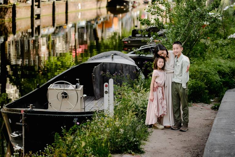 Family with two children standing by an Amsterdam canal next to a small boat, surrounded by greenery during a summer photo session.