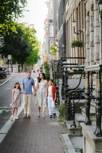 Family strolling together on a classic Amsterdam sidewalk with brick buildings, iron railings, and trees, capturing natural movement and connection during a family photo shoot.