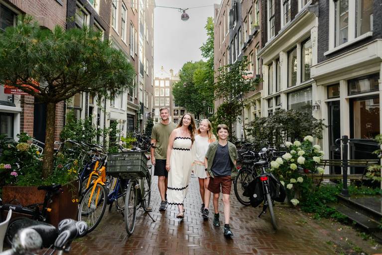 Family walking down a quiet Amsterdam street lined with bicycles, greenery, and historic canal houses on a summer day.