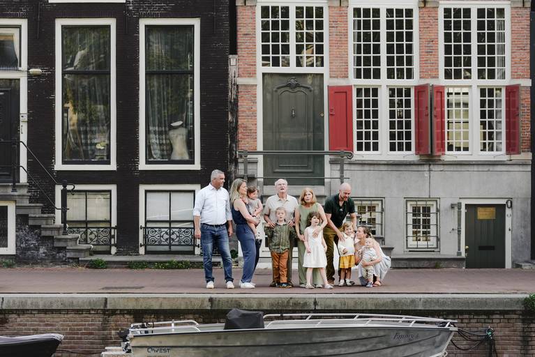 Extended family standing together along an Amsterdam canal, with historic canal houses and a boat in the foreground.