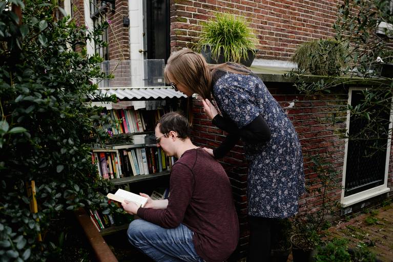 Couple visiting a small book-exchange corner in Amsterdam during a walking photo tour, one of the unique things to do in the city.