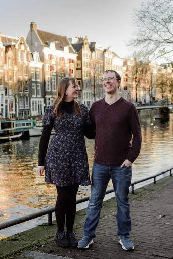Couple smiling by the canal houses in Amsterdam during a relaxed photo session, ideal for travelers wanting memorable trip pictures.