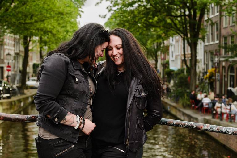 Couple laughing together by an Amsterdam canal during their vacation photoshoot, a popular activity for travelers visiting the city.