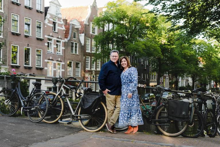 Couple posing on a bridge with Amsterdam’s canal houses and bicycles, showing a classic view for travelers exploring the city.