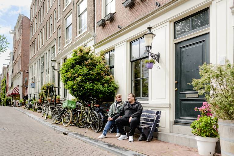 Couple sitting on a bench outside historic canal houses in Amsterdam during a relaxed photoshoot.