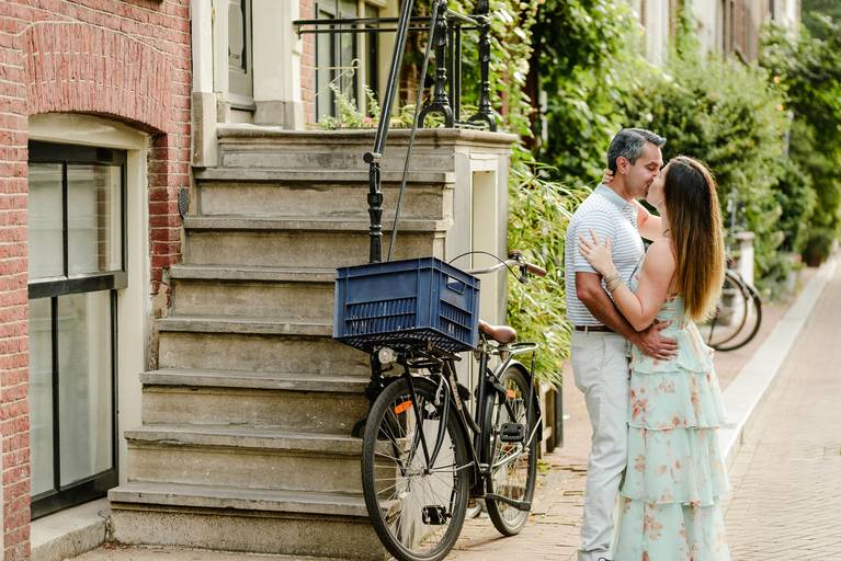 Couple sharing a kiss near a traditional Amsterdam staircase and bicycle during their photo session.