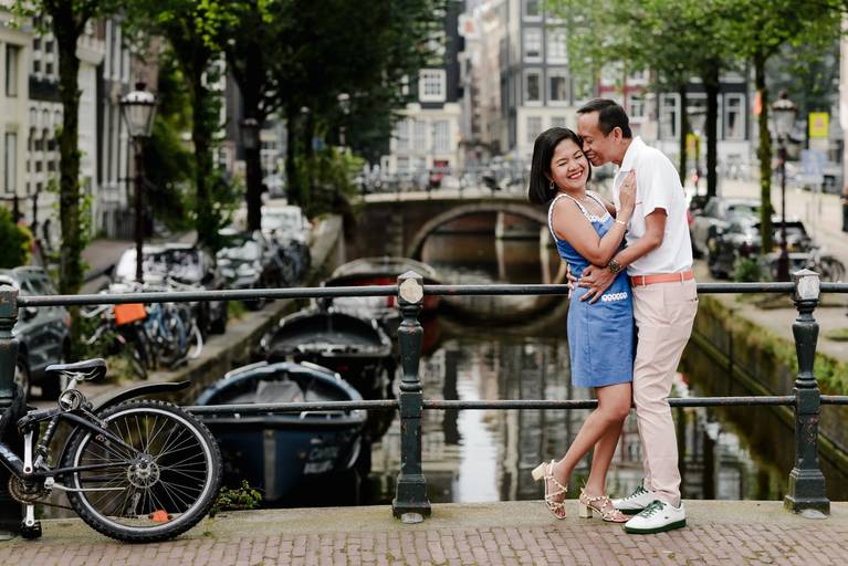 Couple standing on a bridge in Amsterdam during their vacation, capturing a romantic moment with canal views.