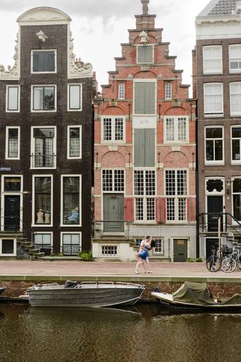 Couple embracing by Amsterdam’s canal houses, enjoying a romantic photoshoot while exploring the city.