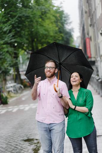 Couple walking with an umbrella during light rain in Amsterdam, laughing together.