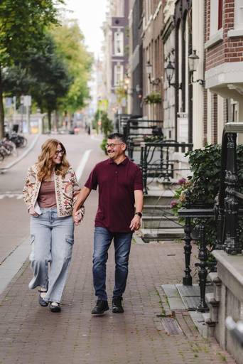 Couple walking through a residential Amsterdam street, smiling at each other during a vacation photoshoot.