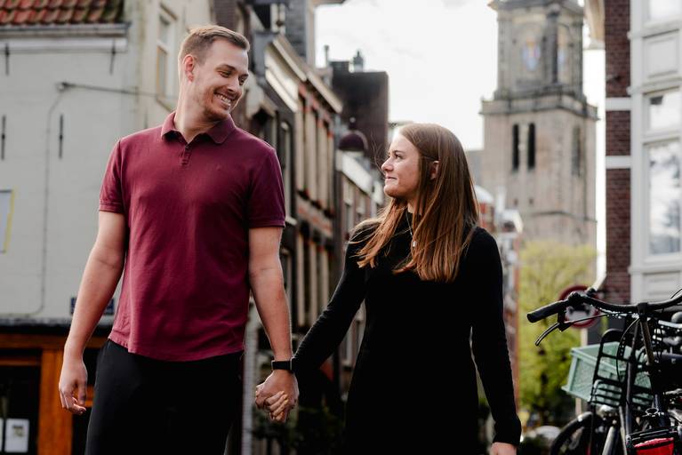 Couple holding hands and walking through historic streets near the Westerkerk in Amsterdam, captured during a vacation photo session.