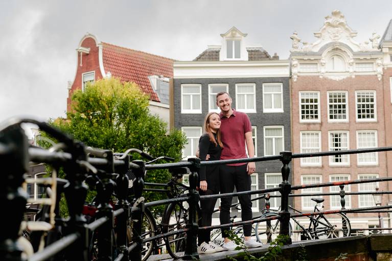 Couple standing on a bridge in Amsterdam’s canal district, enjoying a photography session while exploring the city.