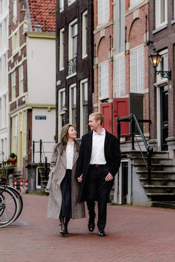 Couple walking through a historic Amsterdam street during their vacation photo session, a popular activity for couples visiting the city.