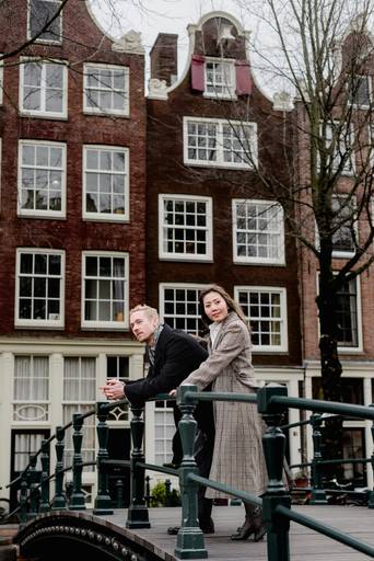 Couple leaning on a canal bridge in Amsterdam, taking in the view during a professional photoshoot on their trip.