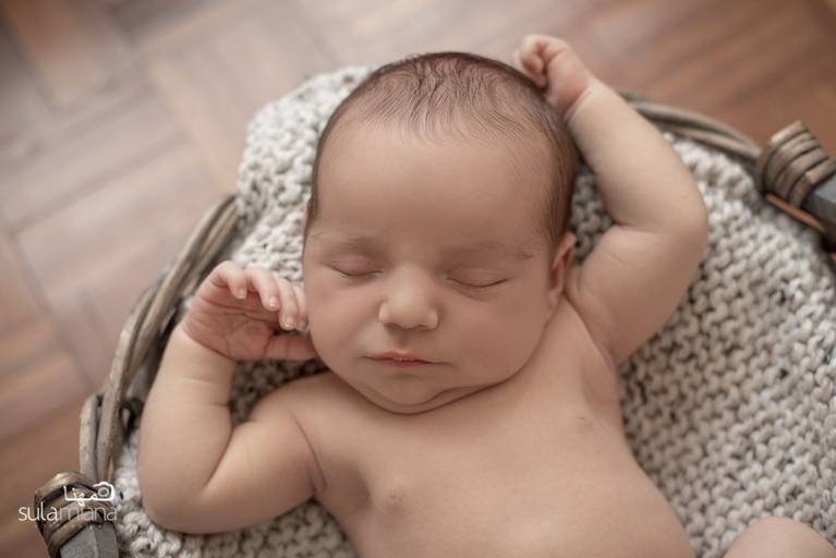 bebê Newborn deitado em cesto com os braços para cima