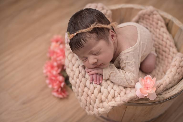 bebê Newborn deitado em cesto com detalhes de flores rosas