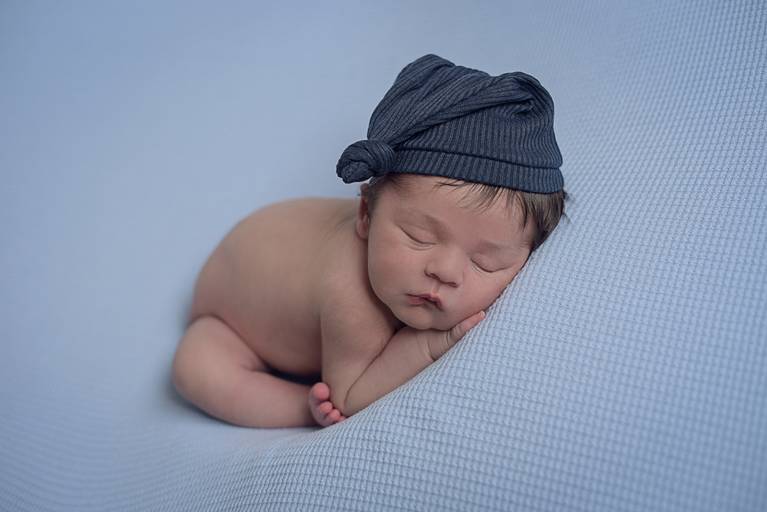 bebê Newborn na pode do no pé no cotovelo e touca azul