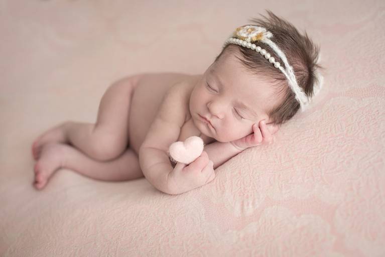 bebê Newborn na pose lateral segurando um coração