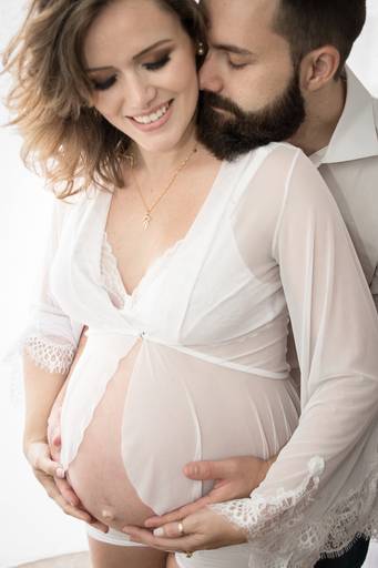 Gestante de lingerie branca abraçada com o marido