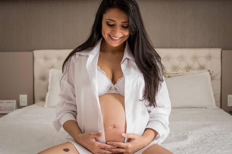 Gestante com blusa branca sentada na cama