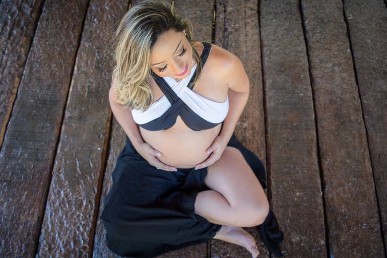 Gestante sentada no chão de dormentes com roupa preta e branca