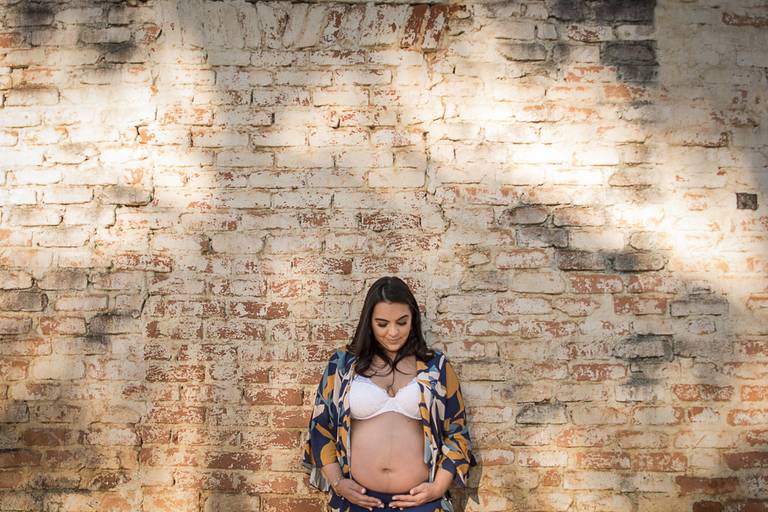 Gestante abraçando a barriga em frente parede de tijolo antiga