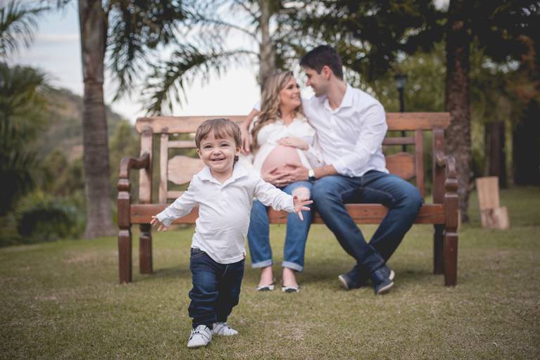 gestante com o marido sentados no banco e filho mais velho correndo