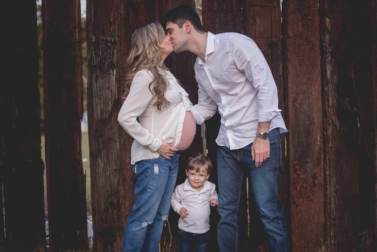 gestante e pai se beijam e filho mais velho no meio dos dois