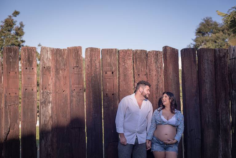 Gestante e marido de mão dadas em frente a parede de dormentes