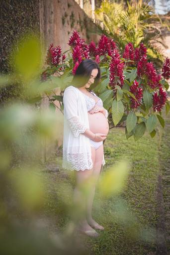 Gestante com lingerie branca no meio do verde e flores vermelhas