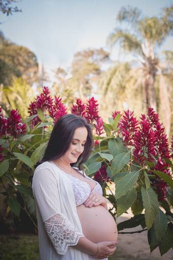 Gestante com lingerie branca no meio do verde e flores vermelhas