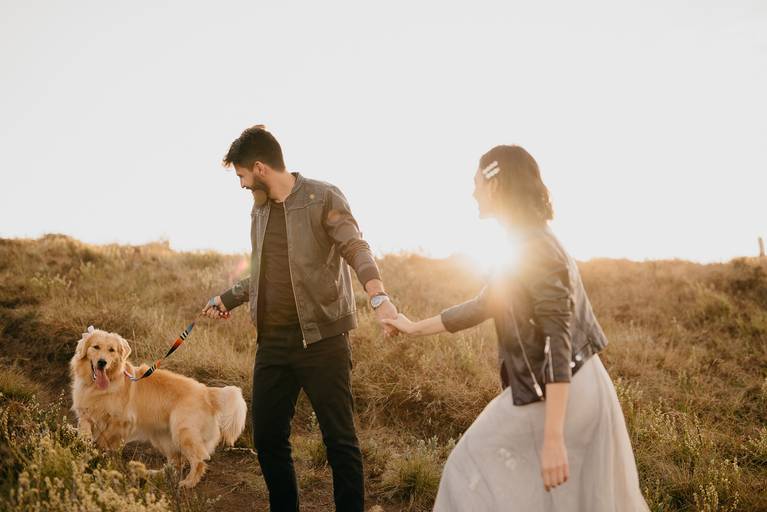Casal no pôr do sol com um golden retriever. 