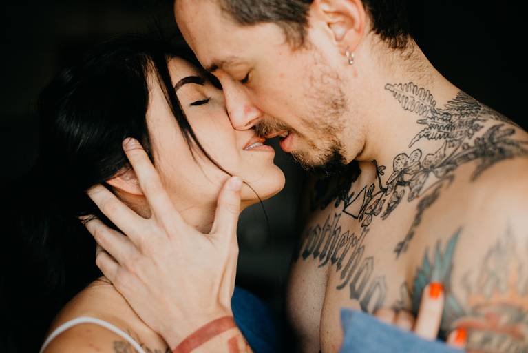 casal tatuado, noivo sem camisa segurando a noiva pelo rosto, trazendo para perto e um quase beijo muito apaixonados. 