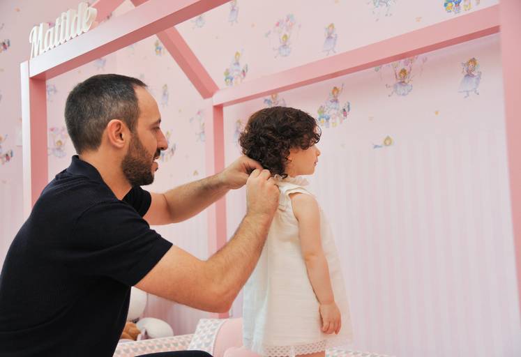 Pai a vestir menina dia do batizado pai e filha cama cor de rosa