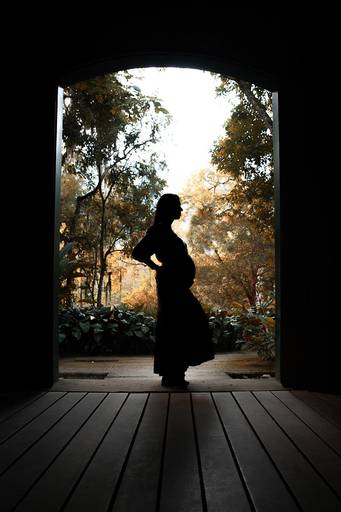 Silhueta de gestante com barriga em destaque no jardim botânico, durante o pôr do sol.