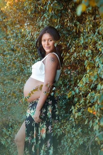 Foto de gestante sozinha em ensaio no meio da natureza verde.