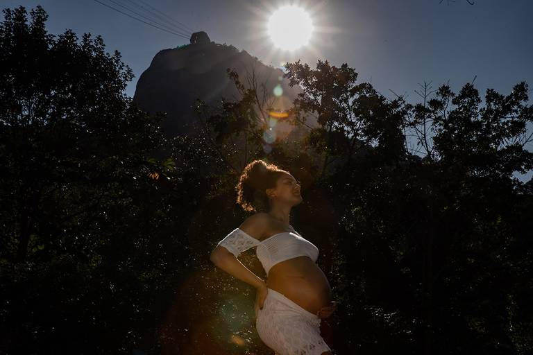 Gestante sorrindo com paisagem verde e montanhas do Rio ao fundo.