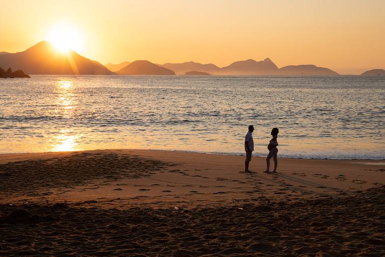 Silhueta de casal de gestantes de mãos dadas com o sol nascendo ao fundo.