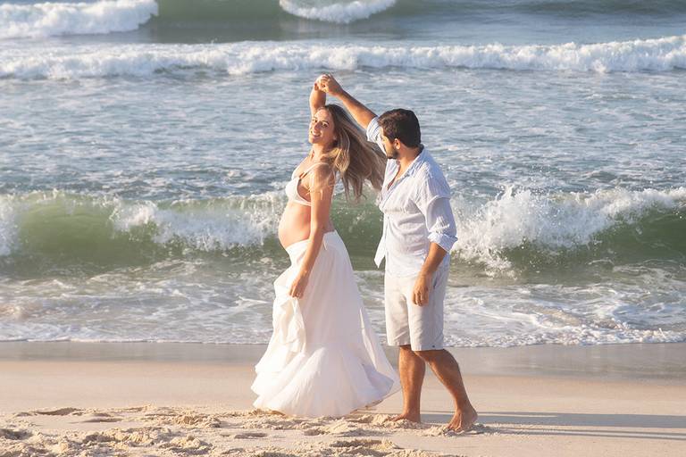 Casal de gestante sorrindo e se divertindo durante ensaio na praia.