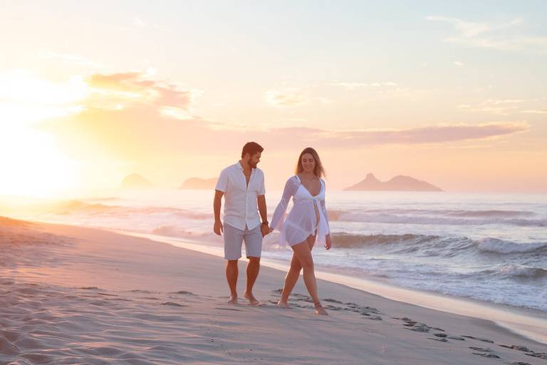Casal de gestante andando na areia da praia no início da manhã.