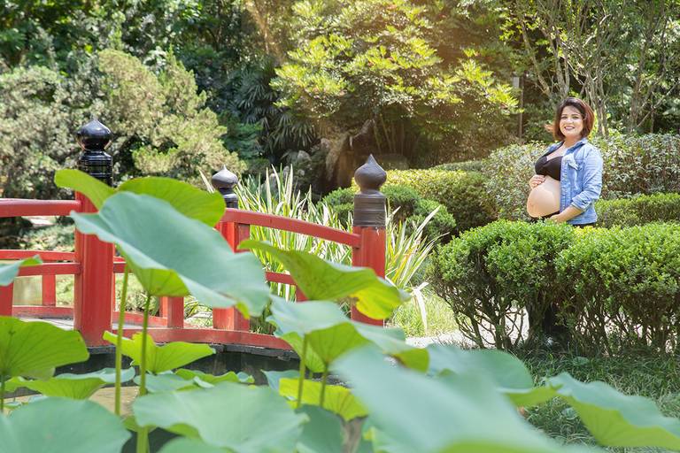 Gestante em ensaio no Jardim Botânico, com folhas verdes ao fundo.