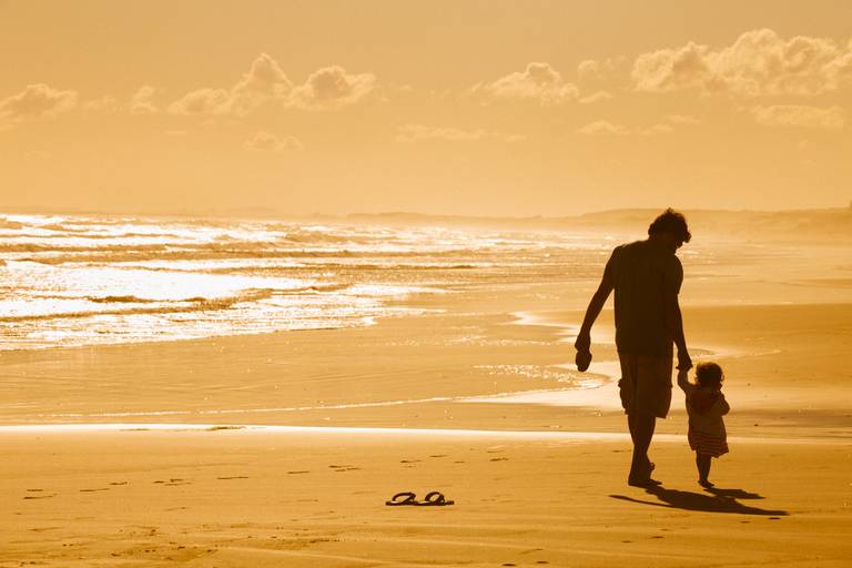 pai caminhando na praia de mãos dadas com a filha