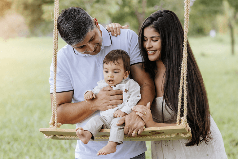 Ensaio externo feito por Alexandra Paz de bebê com família pose no balanço de madeira, em Brasília