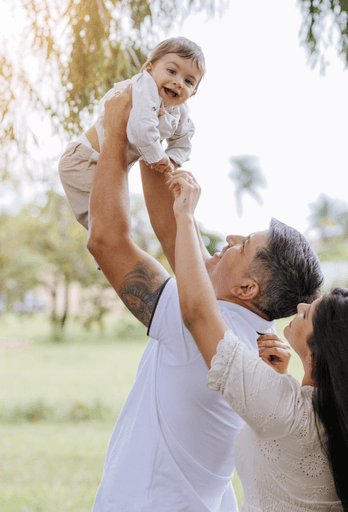 Bebê erguido pelos braços do pai em ensaio externo família, Brasília por Alexandra paz