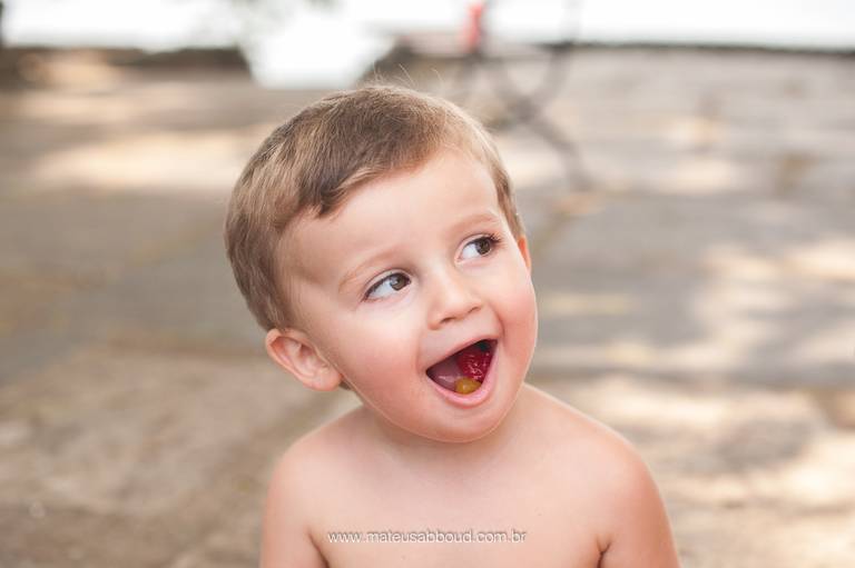 criança sentada chupando bala com a boca aberta em ensaio de familia na fortaleza de santa cruz em niterói no rio de janeiro