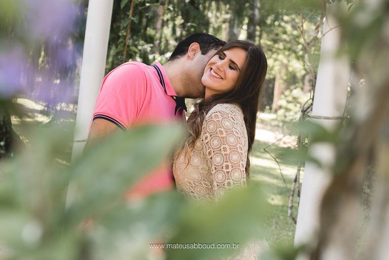 casal de noivos com o noivo beijando o pescoço da noiva e a noiva feliz e sorrindo no jardim botânico no rio de janeiro
