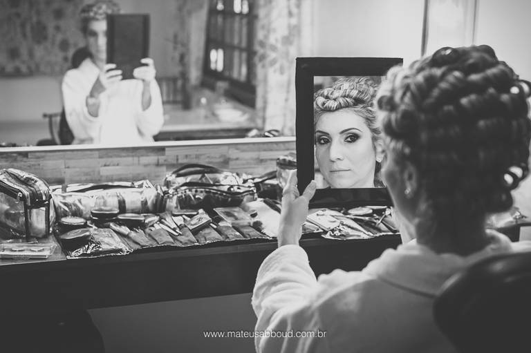foto em preto e branco da noiva no making of se olhando em um espelho de mão