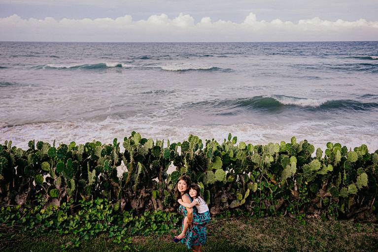 Mãe levando a filha nas costas com o mar de fundo.