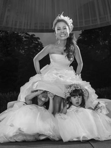 Foto de uma noiva oriental, descendente de japonesa, onde as daminhas de honrra entream de baixo do vestido dando um ar documental ao registro fotografico social