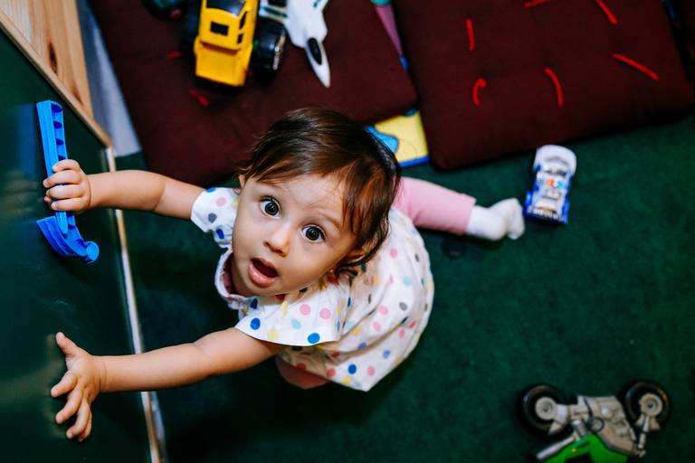 menina sentada no chão brincando segura martelinho de brinquedo e olha para o alto